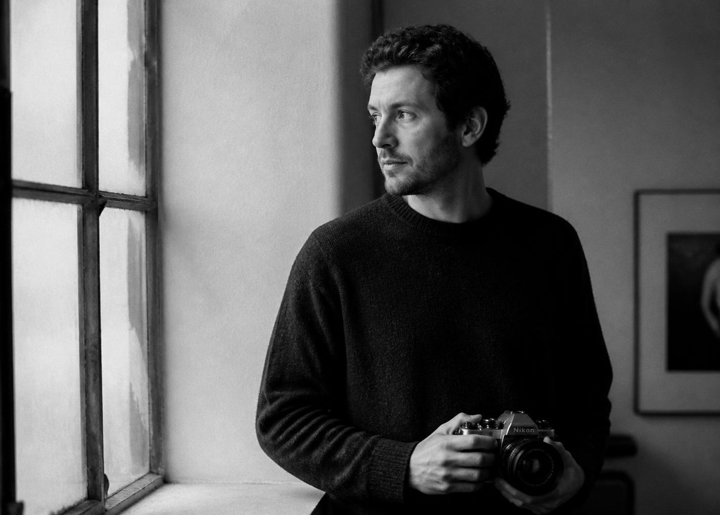 Portrait of photographer Jacopo Stortini holding a film camera by a window